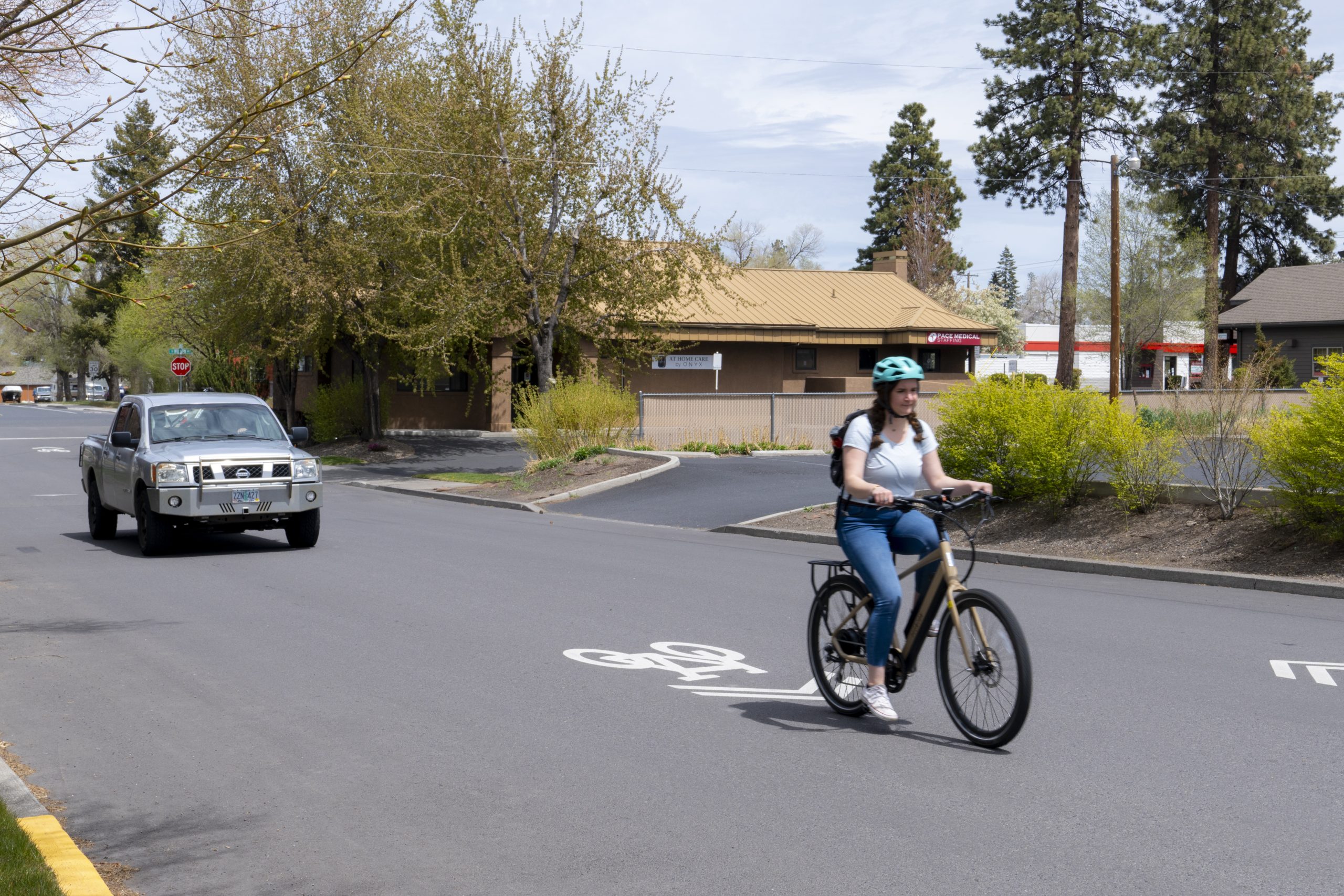 A cyclist riding in a designated bike lane while a car drives on the road in Bend, OR. The scene is related to a safe driving course.