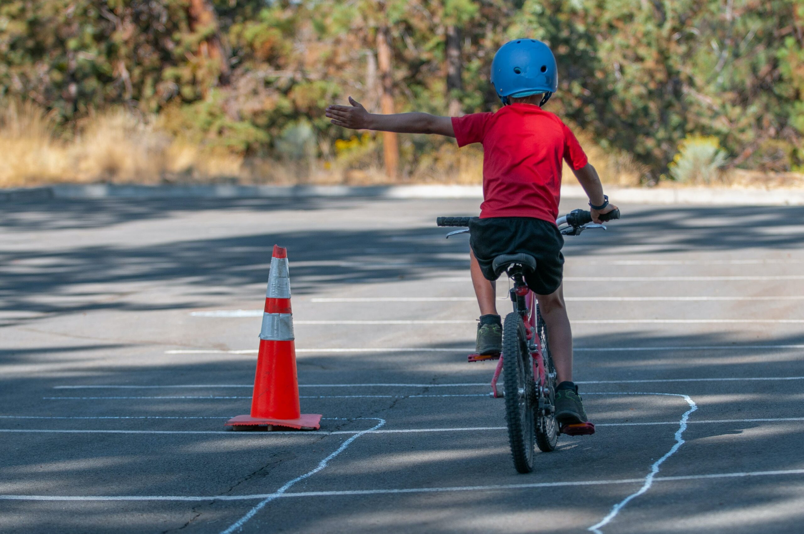 Child practicing hand signals on a bike during a Driver Education Course, navigating around traffic cones.
