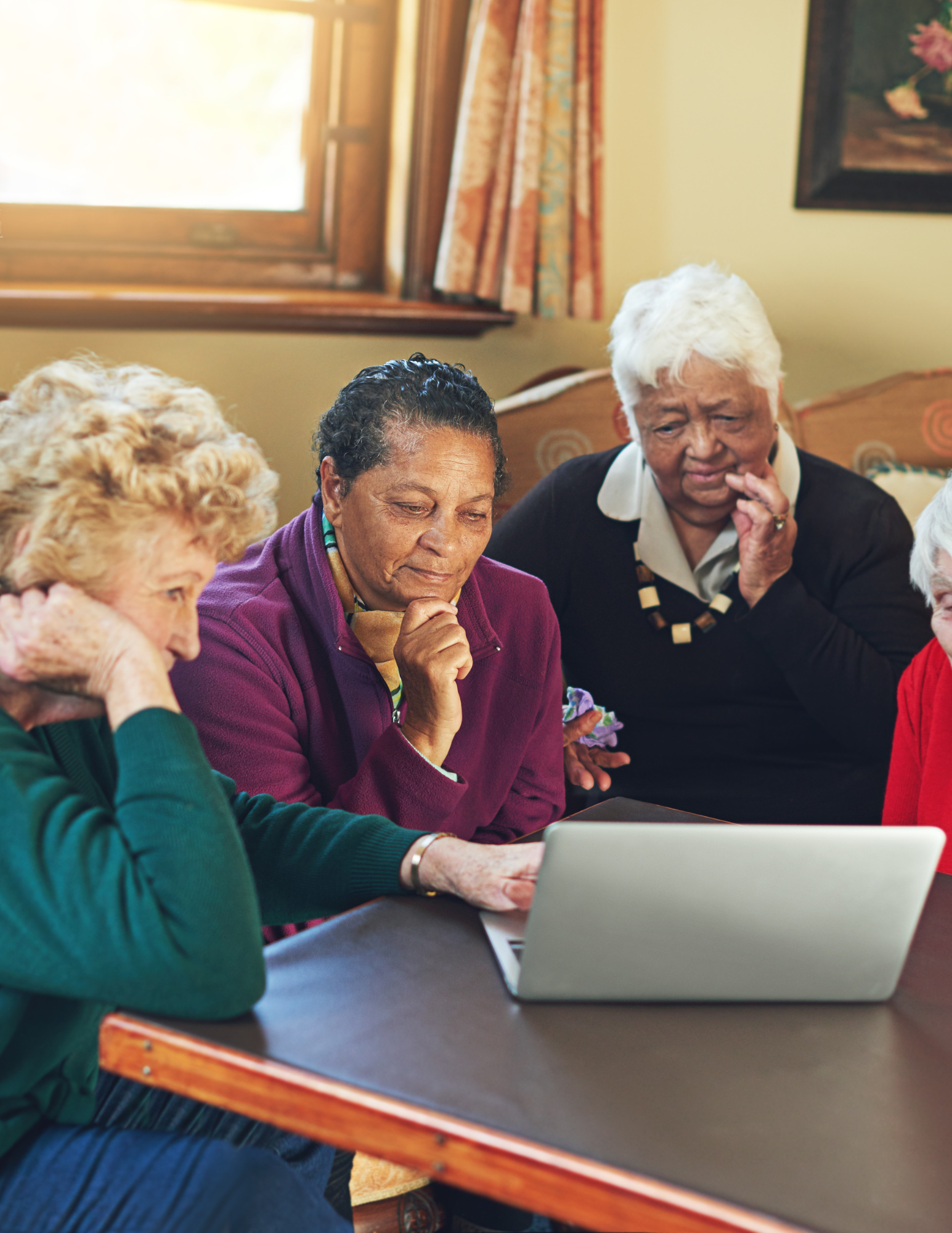 A group of older women gathered around a laptop, engaging with the screen in a room. The scene is related to a driver safety course in Gresham, OR.
