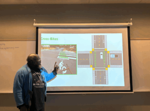 Man pointing at a projected illustration on a whiteboard about traffic road signs.