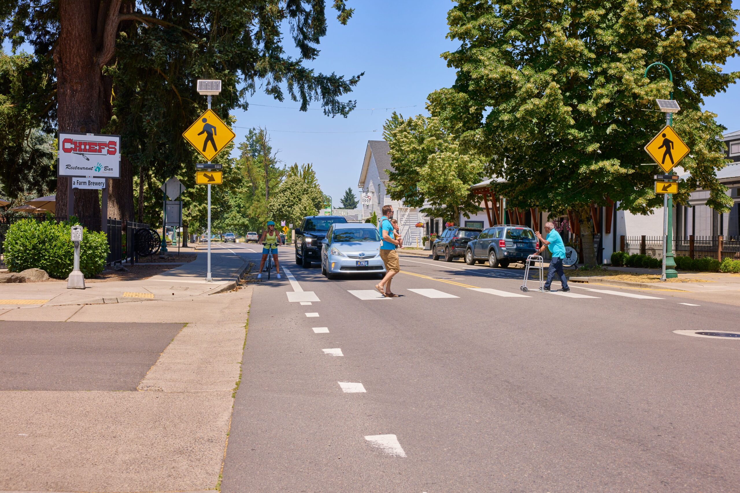 Pedestrians crossing a street at a crosswalk with traffic signs, including a person using a walker, in Gresham, OR. The scene is related to a road safety course in Gresham, OR.