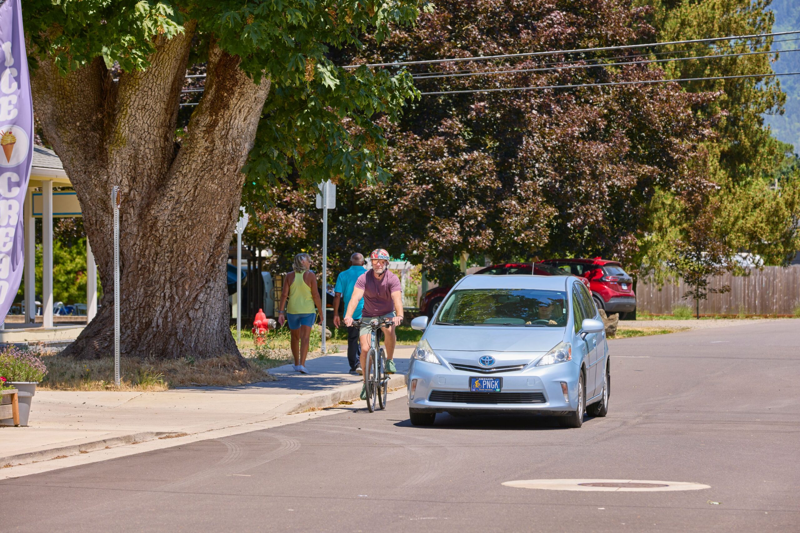 A cyclist riding alongside a car on a street with trees in the background in Oregon. The scene is related to an Oregon friendly driver course.