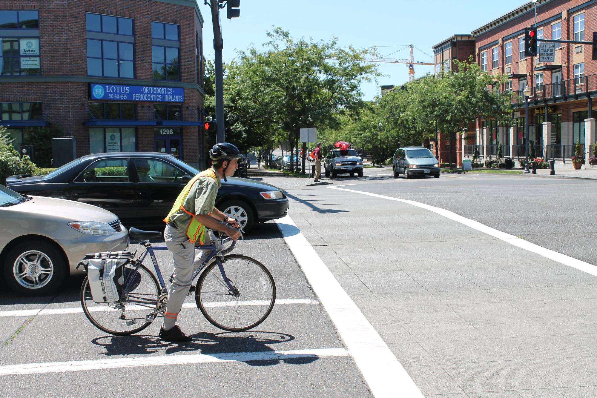 A cyclist walking their bike across a crosswalk while cars are stopped at a traffic light in Oregon. The scene highlights vulnerable road users in Oregon.