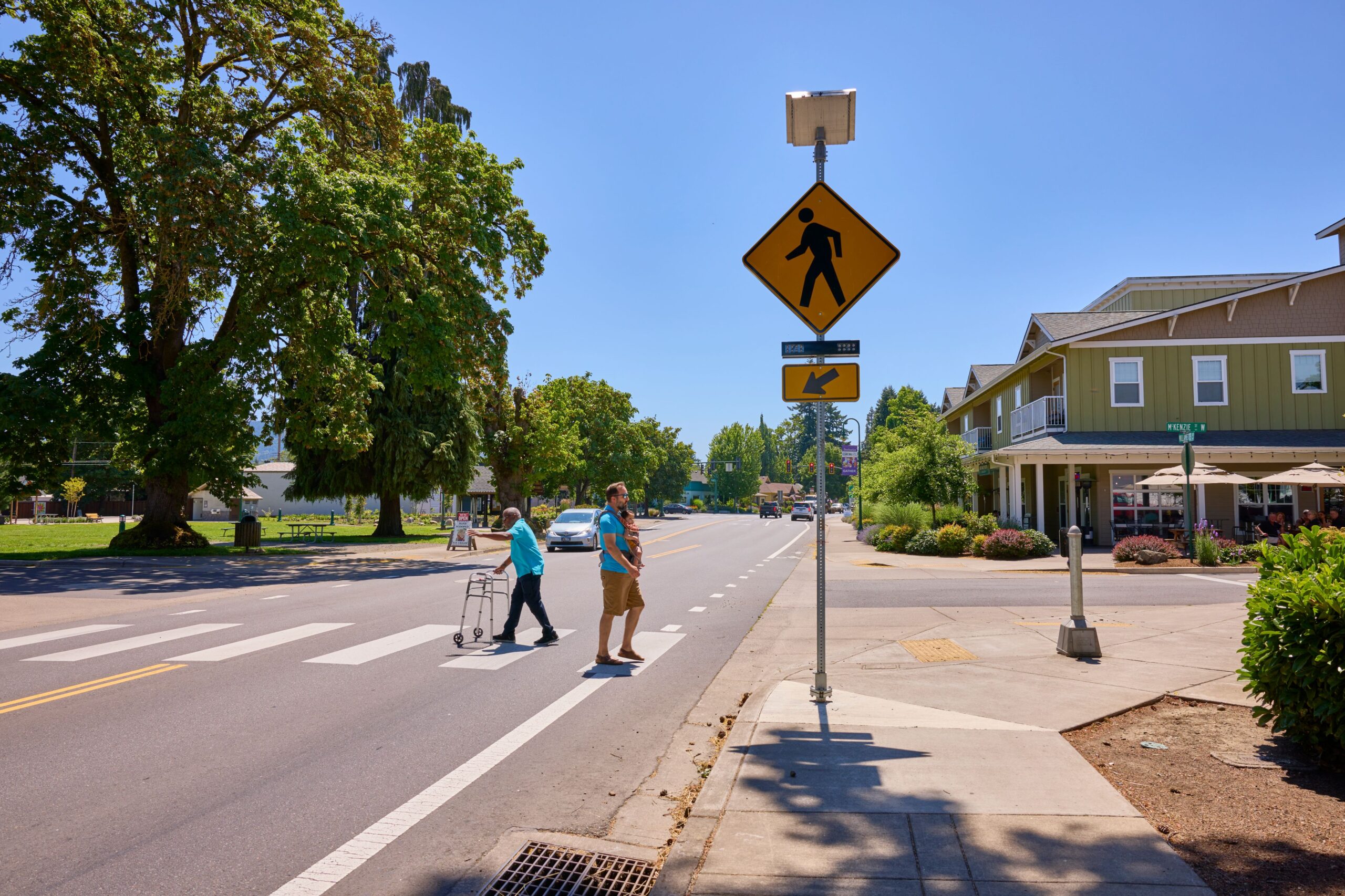 Image showing pedestrians crossing a street with a walking sign, emphasizing the importance of driver safety training for business leaders and teams to improve awareness of pedestrian safety and responsible road-sharing practices.