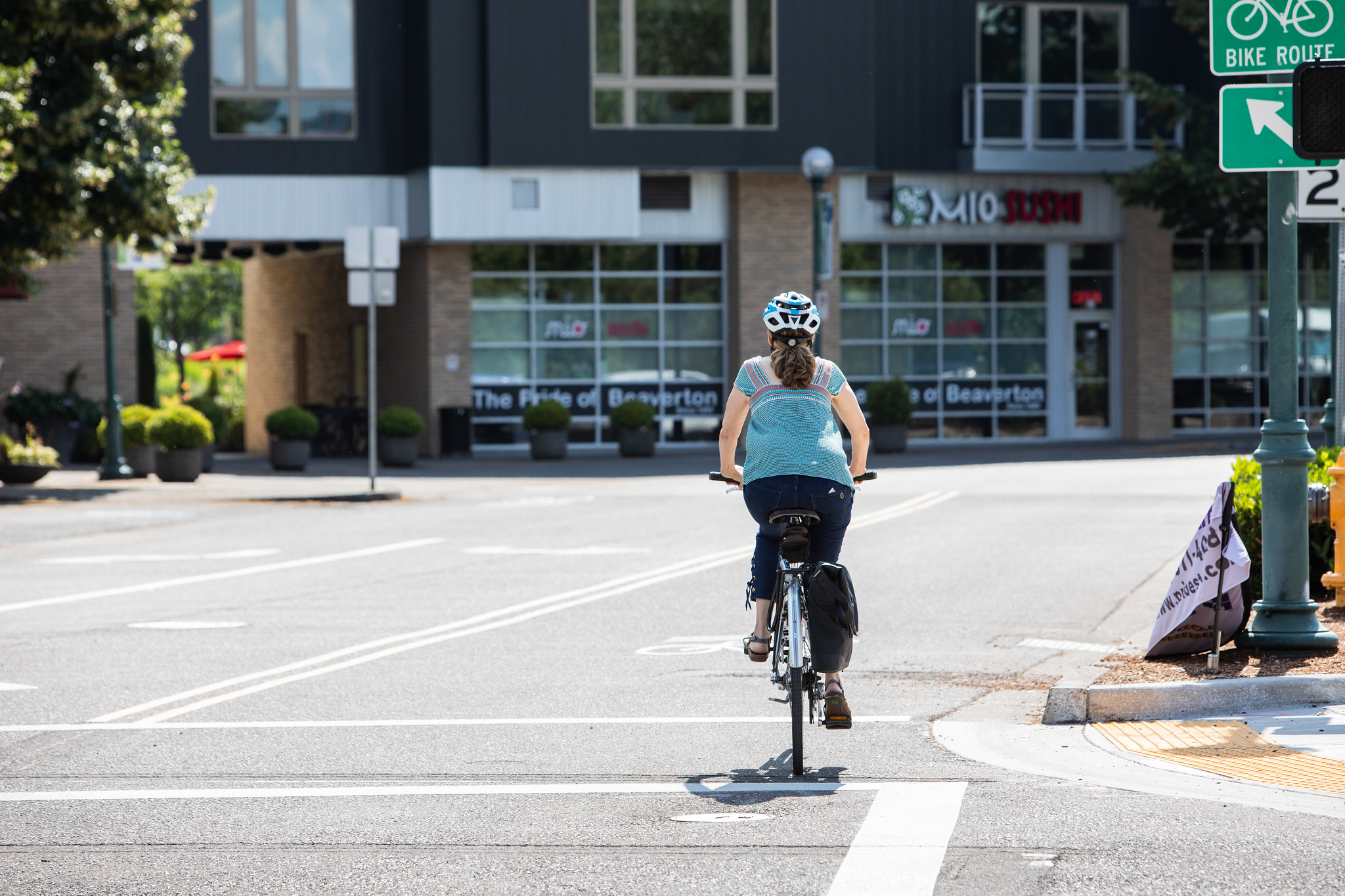 A cyclist riding along a designated bike lane near a commercial area. The image emphasizes the concept of a safe place for cyclists, promoting a safe workplace for all road users by providing proper infrastructure.