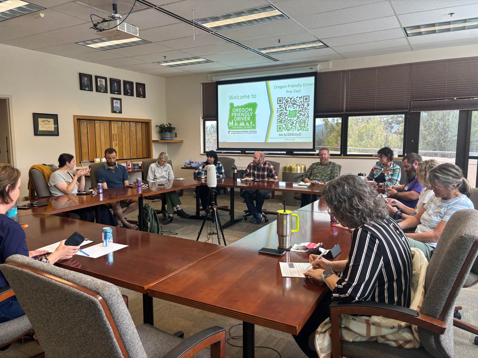 Image showing a group of people gathered around a conference table in a meeting room, engaging in a discussion with a presentation on the screen, highlighting the importance of the OFD course in promoting safety and awareness.