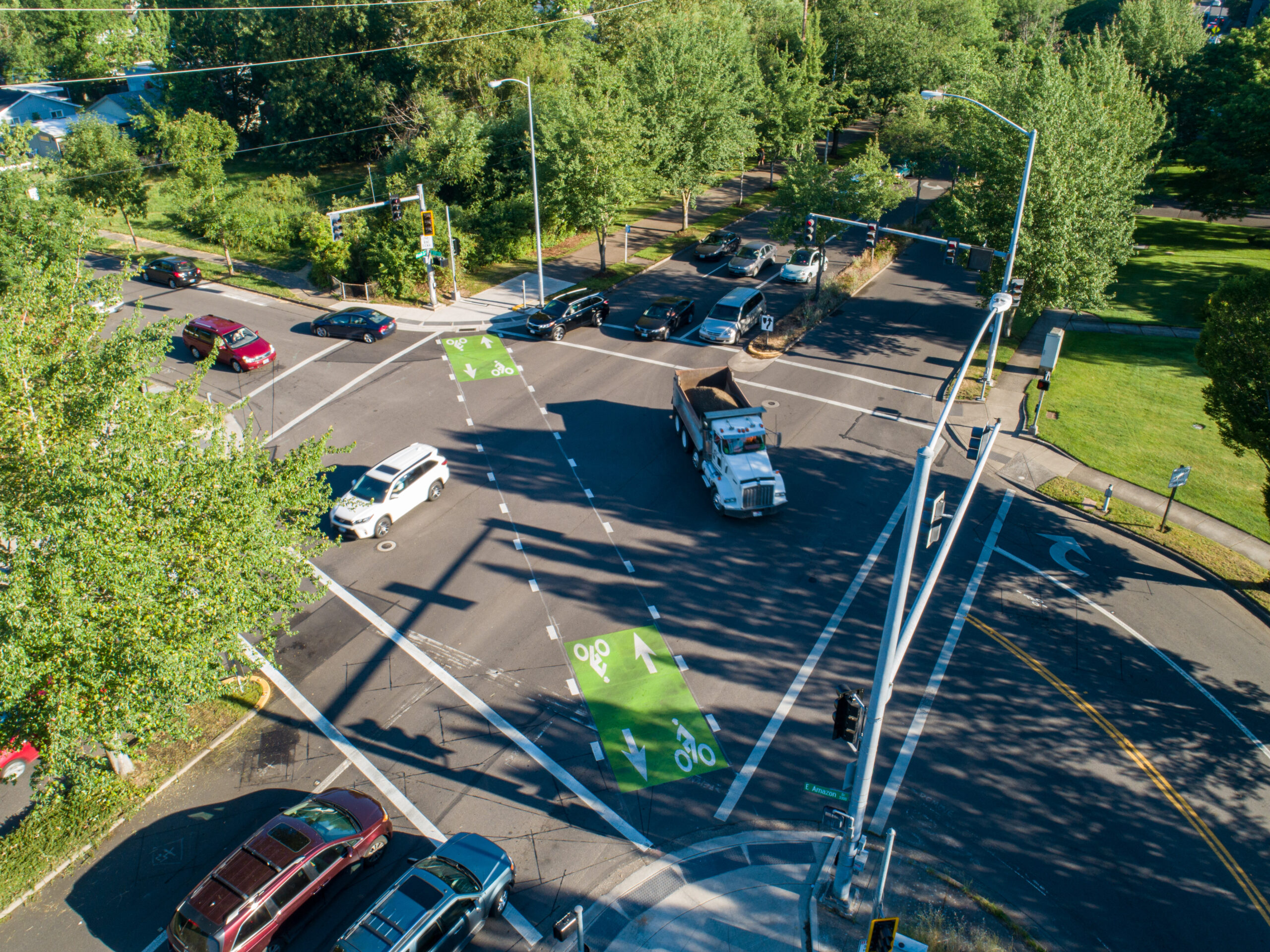 An aerial view of an intersection showing a truck and multiple vehicles, with designated bike lanes visible. The image highlights the interaction between commercial drivers and vulnerable road users, such as cyclists, at a busy urban intersection.