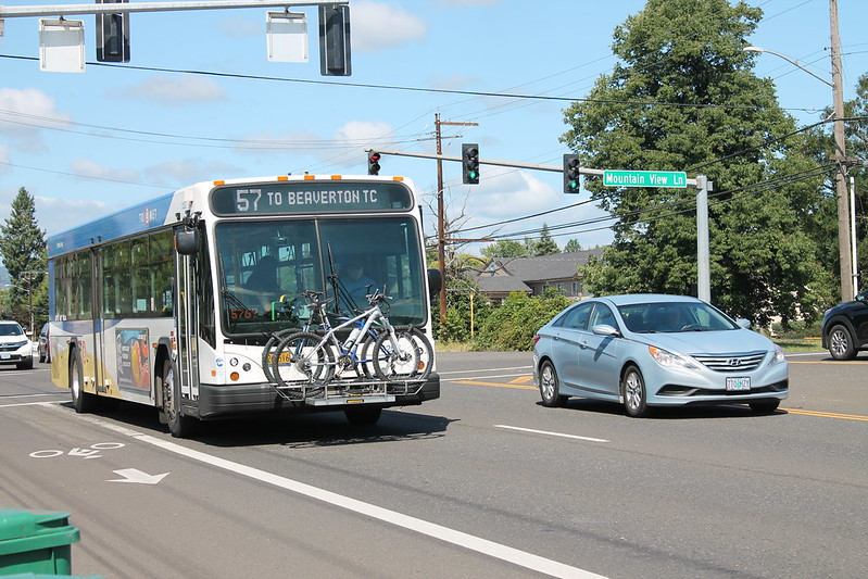 A TriMet public transit bus and a silver sedan travel through a Portland metro area intersection