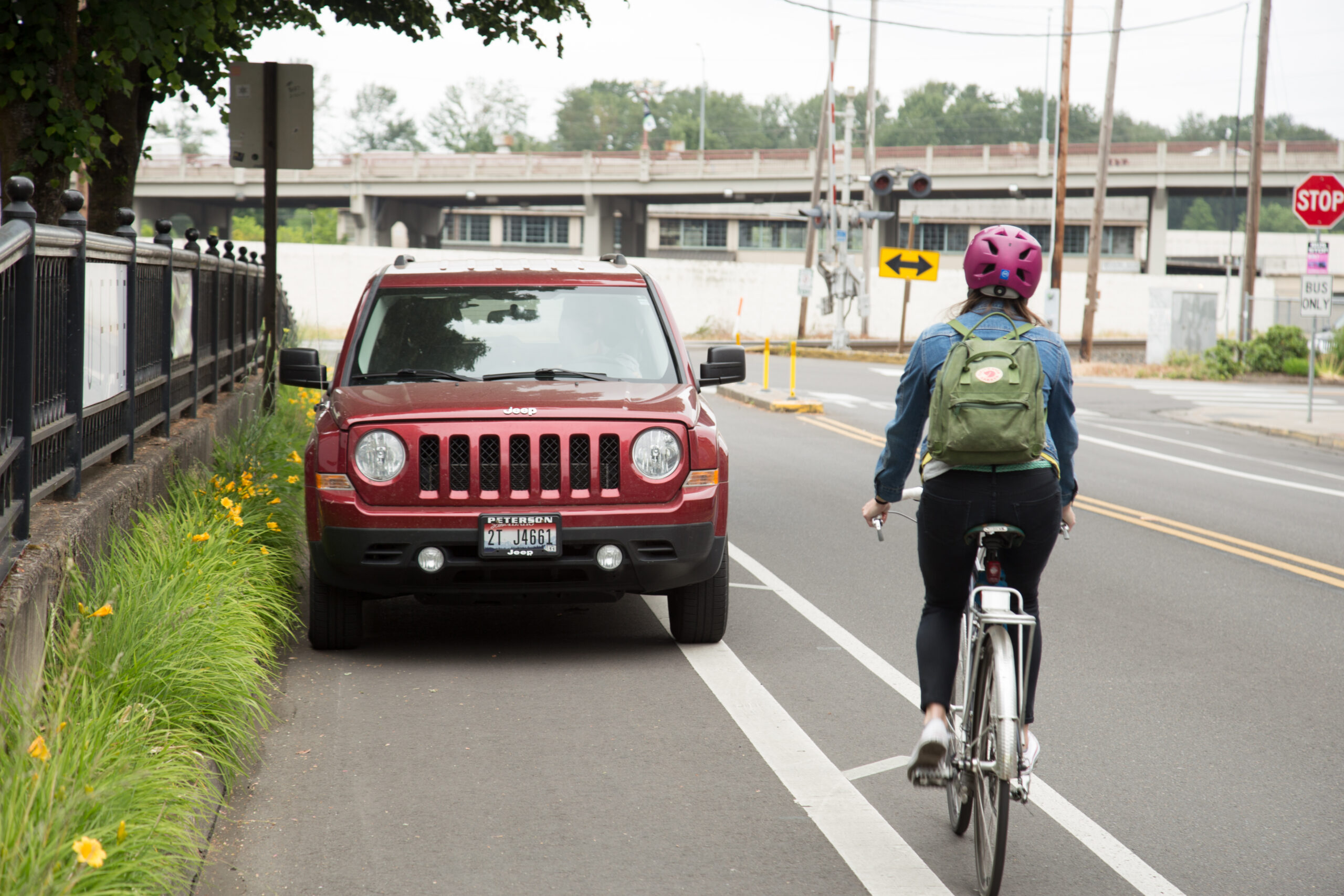 A cyclist rides past a red SUV parked in a marked bike lane